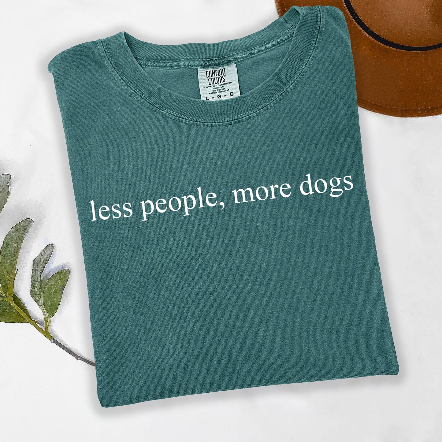 Teal t-shirt with 'less people, more dogs' text on a white background