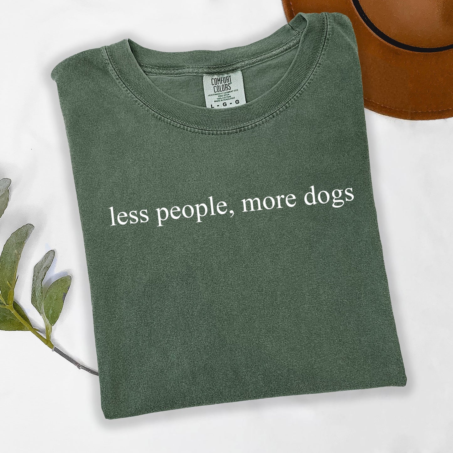 Folded green t-shirt with 'less people, more dogs' text on a white background