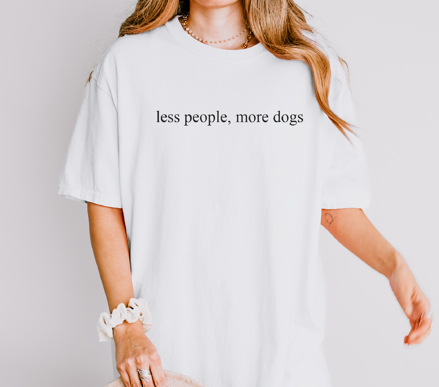 Person wearing a white t-shirt with 'less people, more dogs' text on a plain background