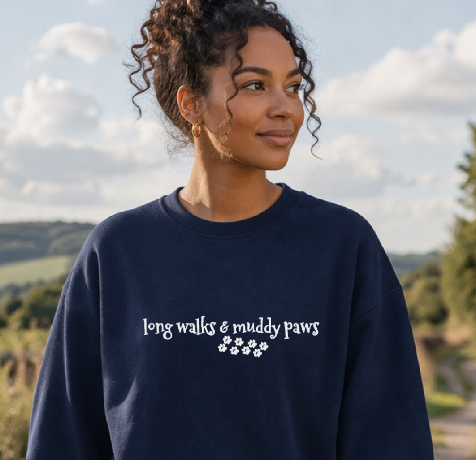 Woman walking a dog on a path with a navy sweatshirt featuring text and paw prints.