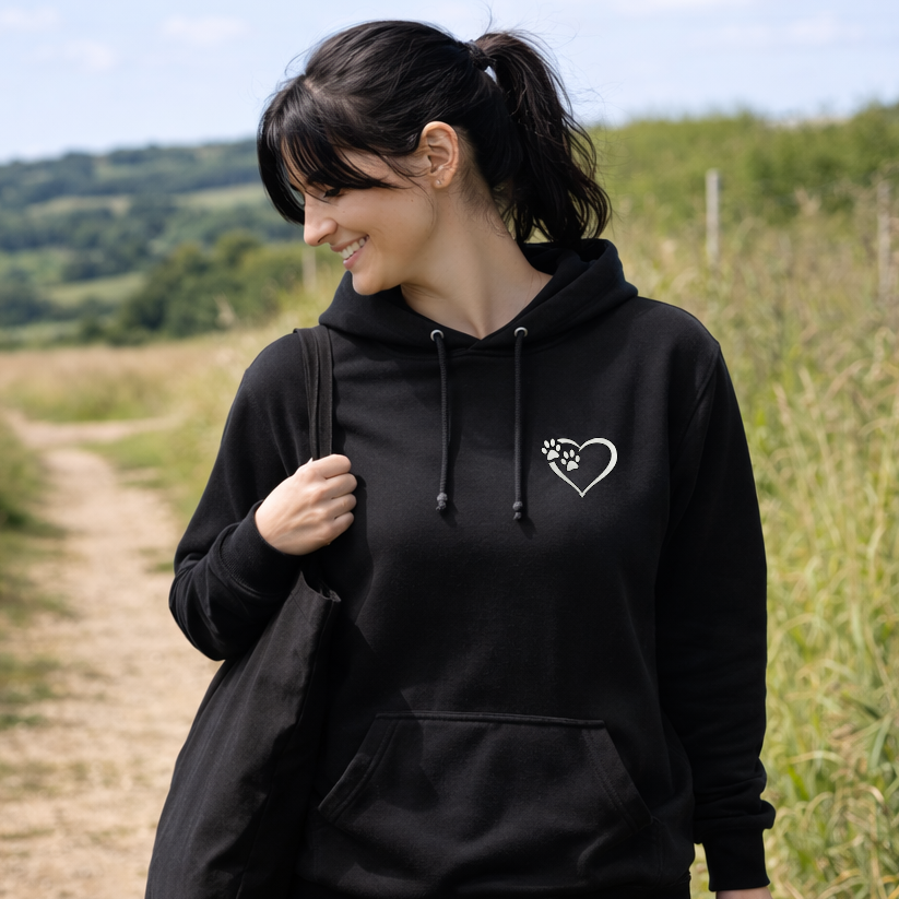 Woman wearing a black hoodie with a heart and paw print design, standing in a field.