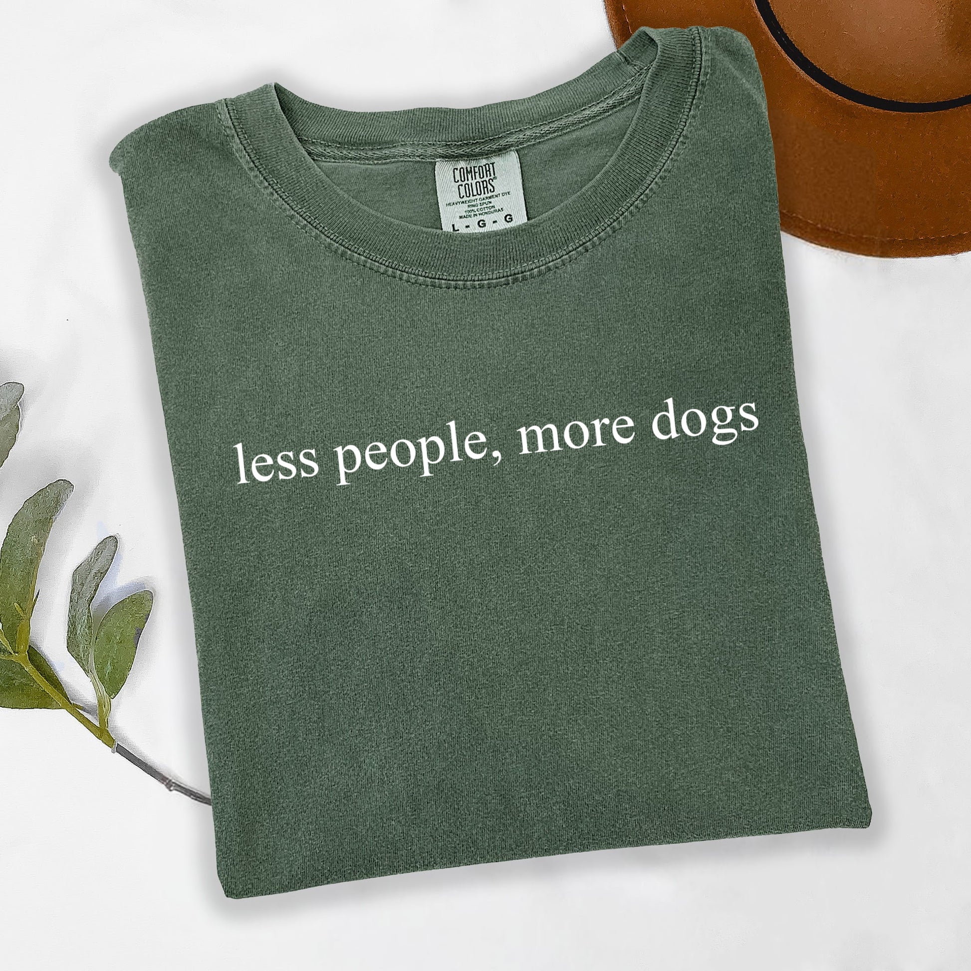 Folded green t-shirt with 'less people, more dogs' text on a white background