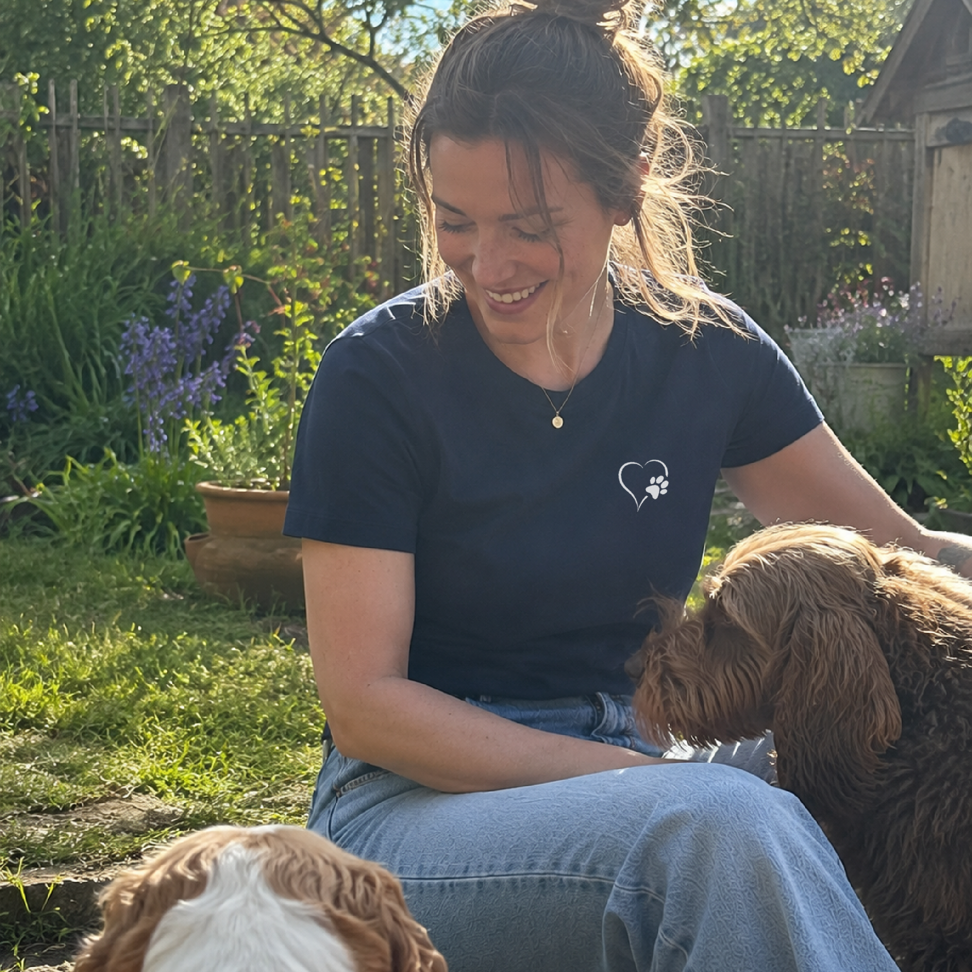 Woman sitting outdoors with two dogs in a garden setting