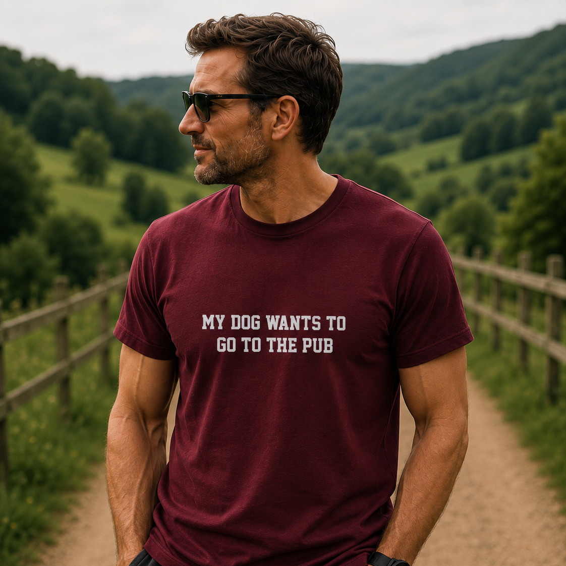 Man wearing a maroon t-shirt with text standing on a path with greenery in the background