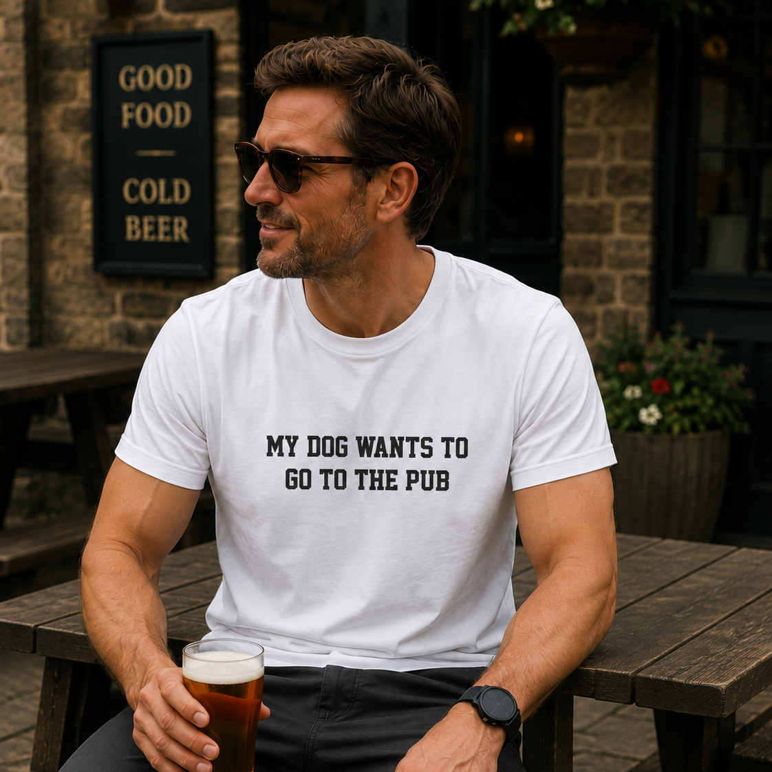 Man sitting at a pub holding a beer, wearing a white t-shirt with text.
