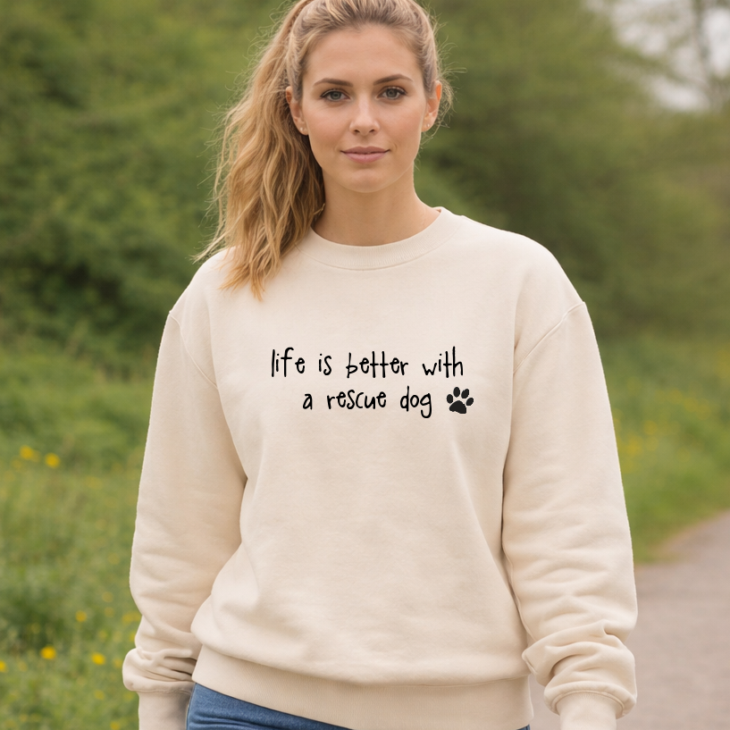 Woman wearing a cream sweatshirt with 'life is better with a rescue dog' text outdoors.
