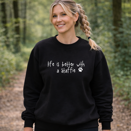 Woman wearing a black sweatshirt with 'life is better with a staffie' text, standing in a forest.