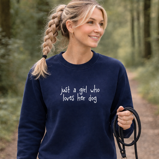 Woman wearing a navy sweatshirt with 'just a girl who loves her dog' text, holding a leash in a forest setting.