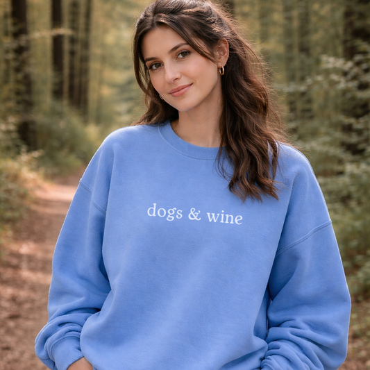 Woman wearing a blue sweatshirt with 'dogs & wine' text in a forest setting