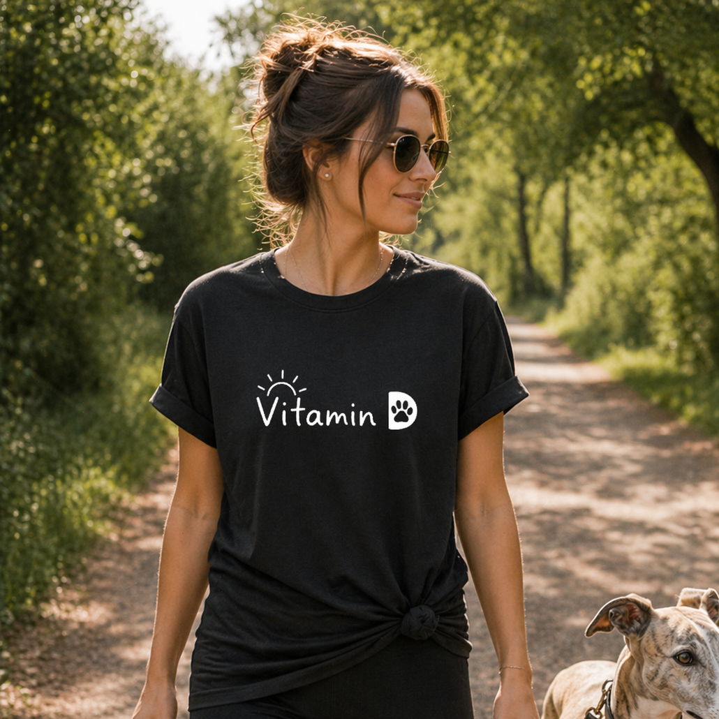 Woman wearing a black t-shirt with 'Vitamin D' logo walking a dog in a park.
