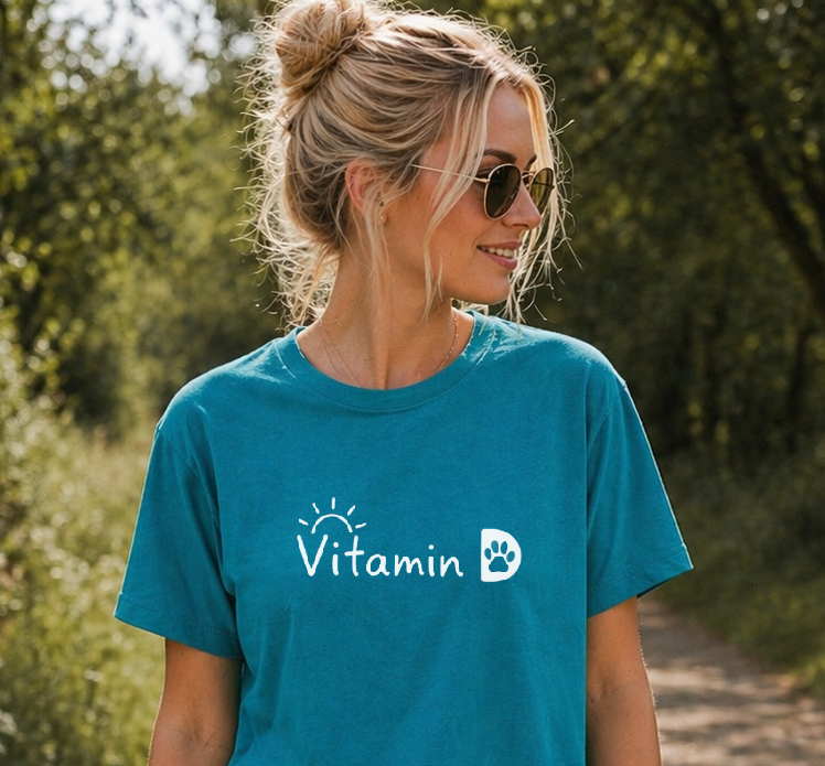 Woman wearing a blue t-shirt with a logo, walking a dog on a path in a park.
