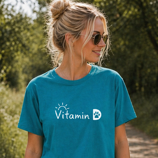 Woman wearing a blue t-shirt with a logo, walking a dog on a path in a park.