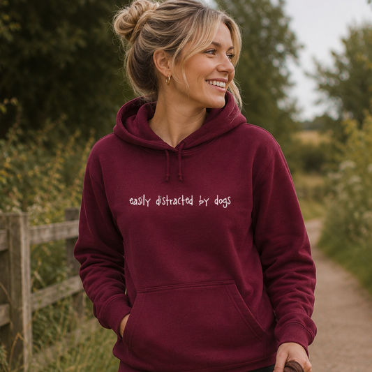 Woman wearing a maroon hoodie with 'easily distracted by dogs' text, standing outdoors.