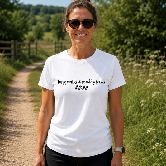 Woman wearing a white t-shirt with 'long walks & muddy paws' text, standing on a path in a natural setting.