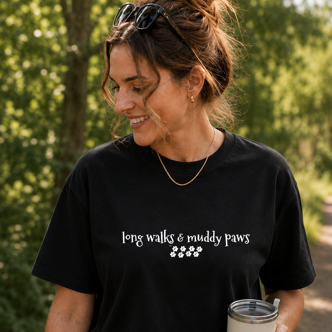 Woman wearing a black t-shirt with 'long walks & muddy paws' text, standing outdoors.