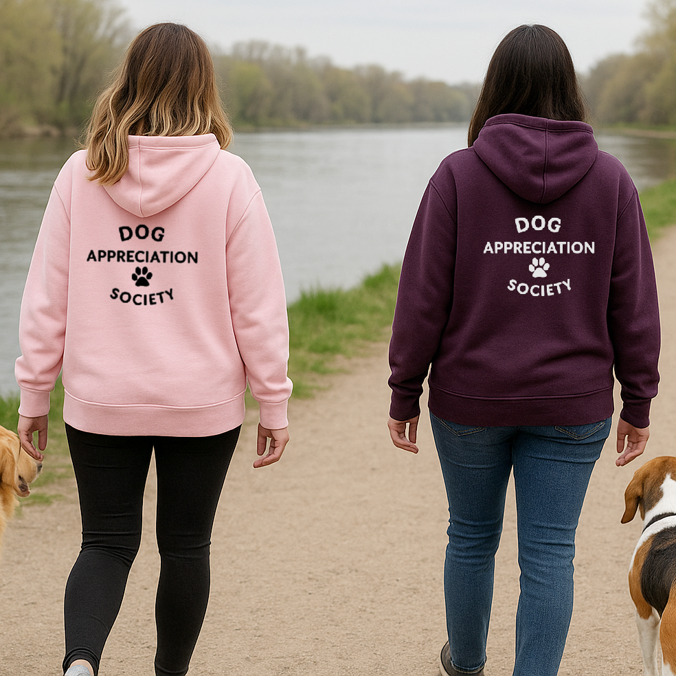 Two people walking with dogs on a path by a lake, wearing hoodies with 'Dog Appreciation Society' text.