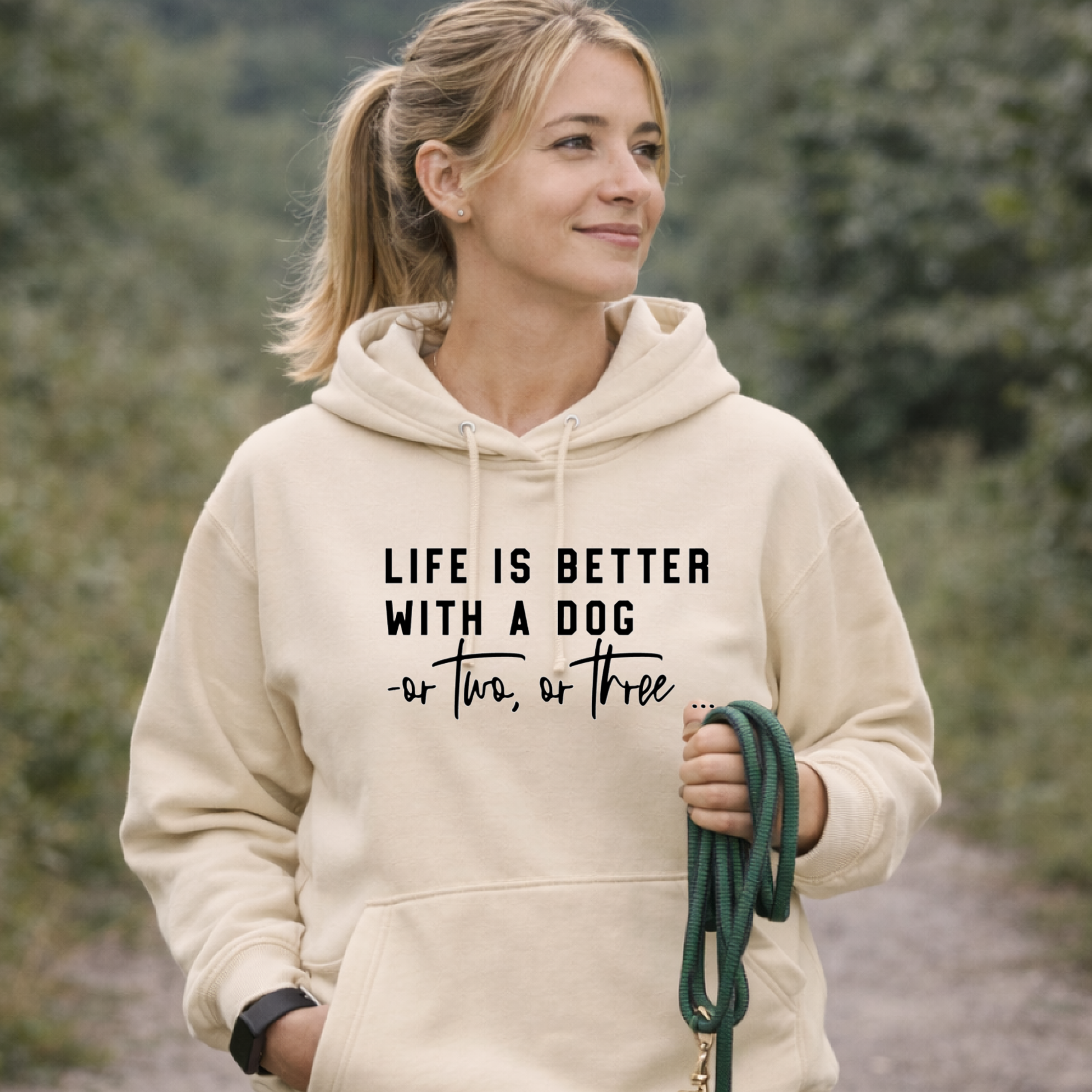 Woman wearing a vanilla hoodie with text holding a leash in a natural setting