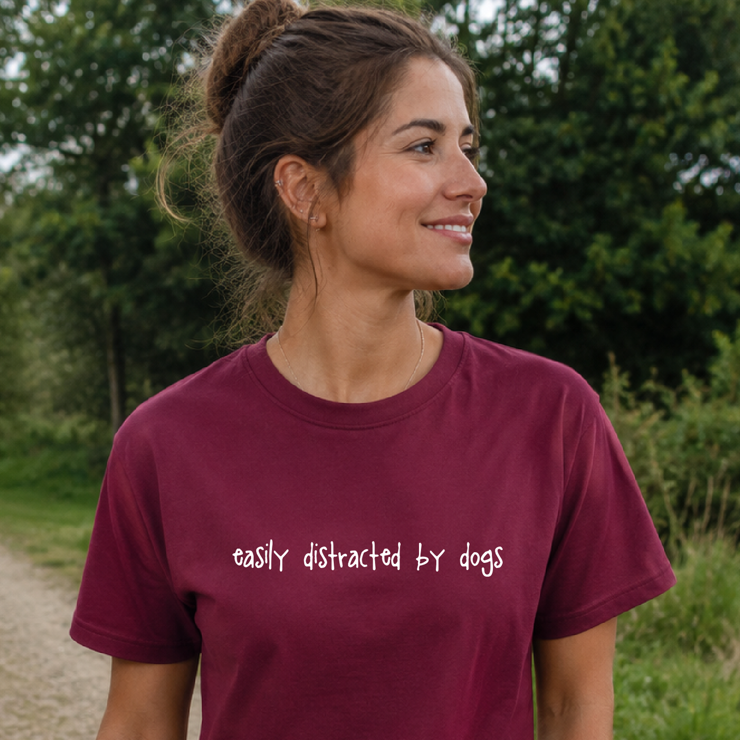 Woman wearing a maroon t-shirt with 'easily distracted by dogs' text outdoors.
