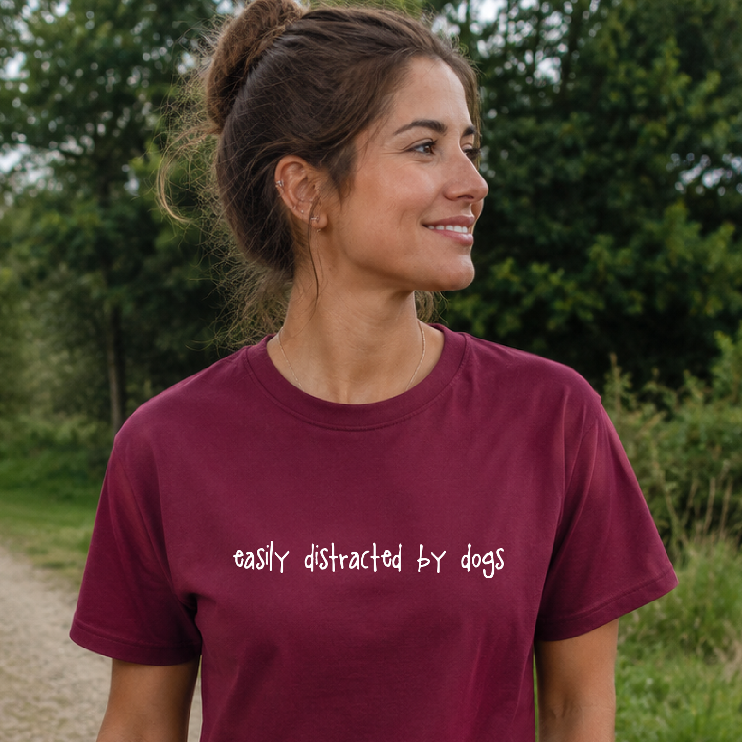 Woman wearing a maroon t-shirt with 'easily distracted by dogs' text outdoors.