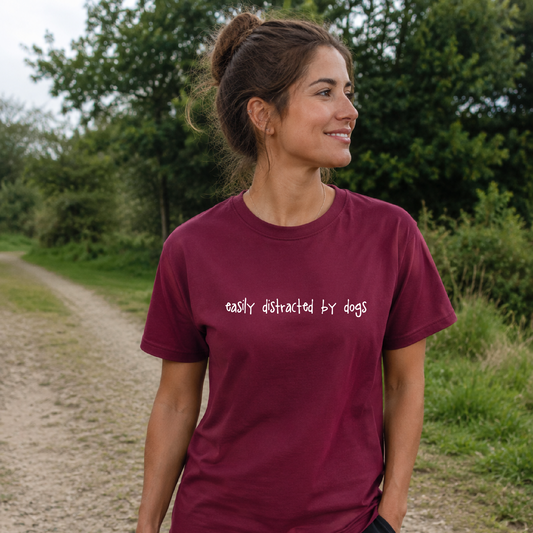 Woman wearing a maroon t-shirt with 'easily distracted by dogs' text outdoors.